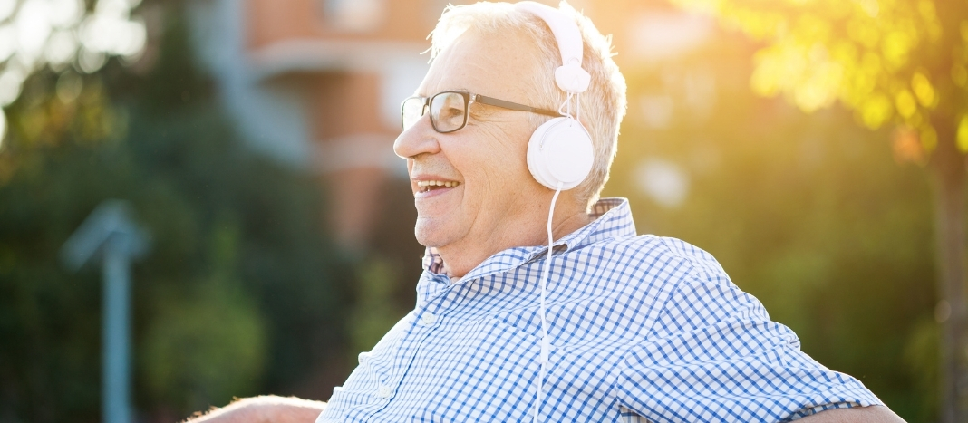 A senior man wearing headphones while sitting on a bench